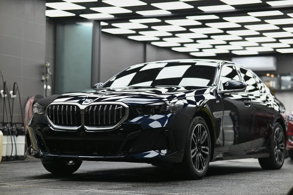BMW 5 系列黑色轎車完工後停在燈箱作業區,車頭 45 度角全車漆面呈鏡面反射|誠美車體美容