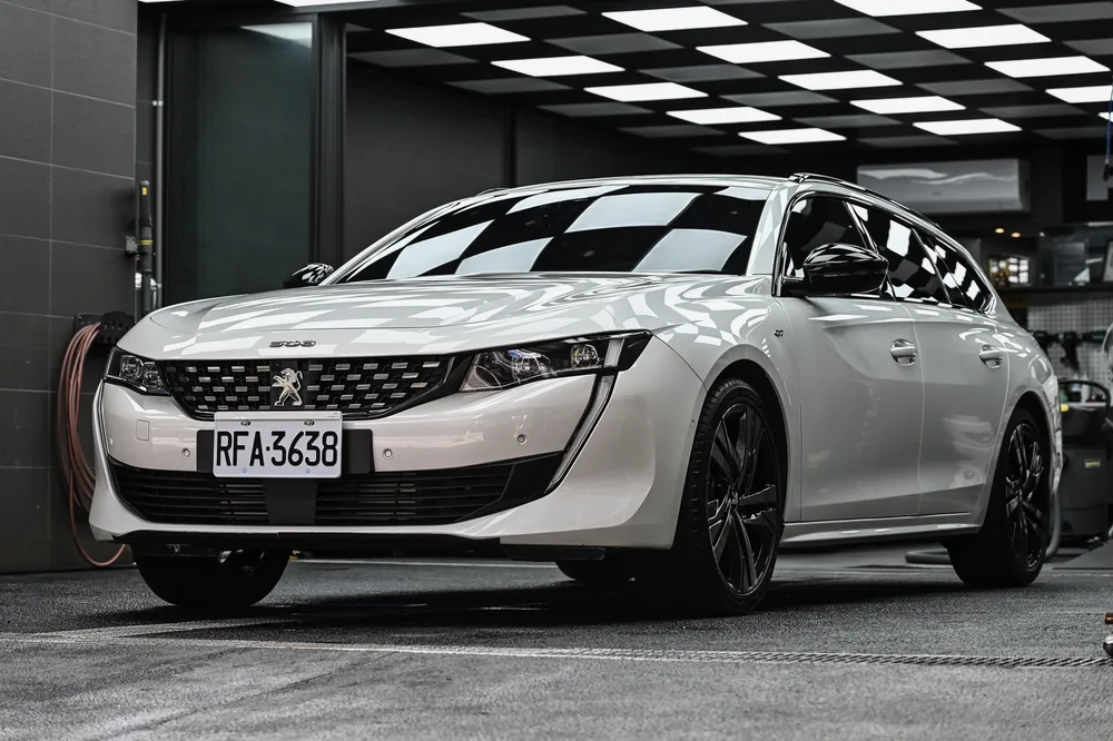 白色 Peugeot 508 SW 完成外觀護理後停於格紋施工區,左前方全景鈑面光澤均勻,誠美車體美容
