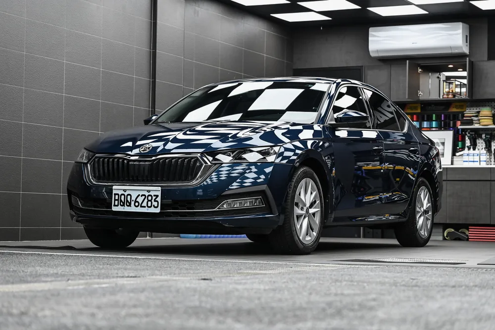 深藍色 Škoda Octavia 完工停放於施工區,車身漆面映出天花棋盤格倒影,誠美車體美容
