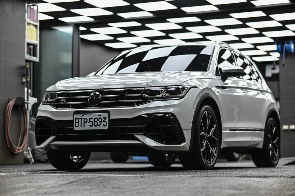 白色 Volkswagen Tiguan 完成精緻打蠟後停於廠內的車頭四分之三視角,車身側面映出棋盤格燈條|誠美車體美容
