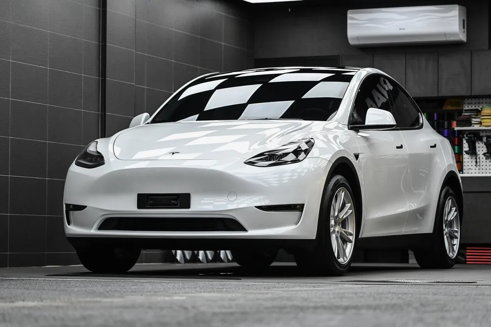 白色 Tesla Model Y 完成雙層鍍膜後,停於施工棚內的左前四十五度車身光澤,誠美車體美容