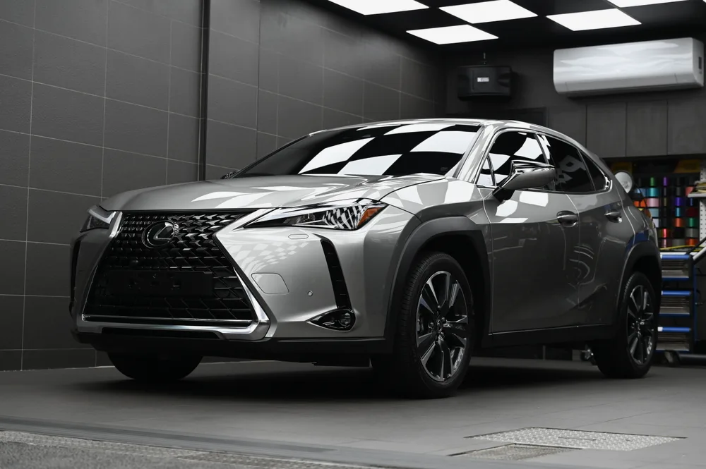 完成雙層鍍膜的銀色 Lexus UX 停在棚拍區,左前方視角車身映出格紋天花板倒影,誠美車體美容