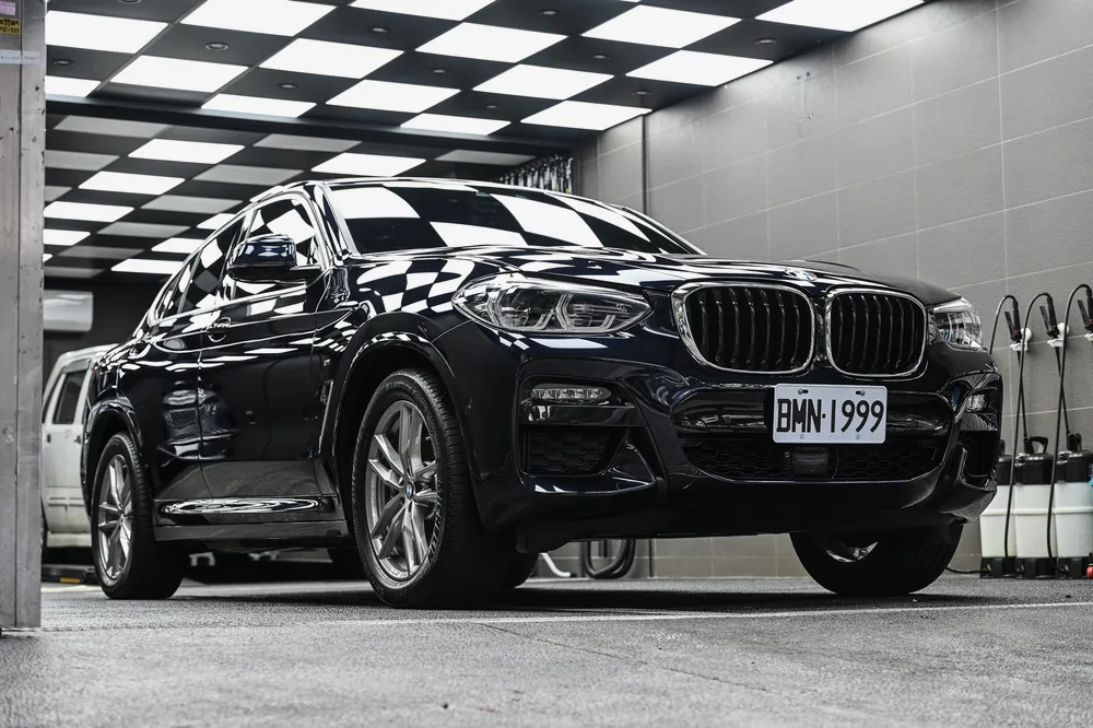 黑色 BMW X4 M Sport 完成基礎護理後停於格紋施工區,左前方全景鈑面映出天花板倒影,誠美車體美容