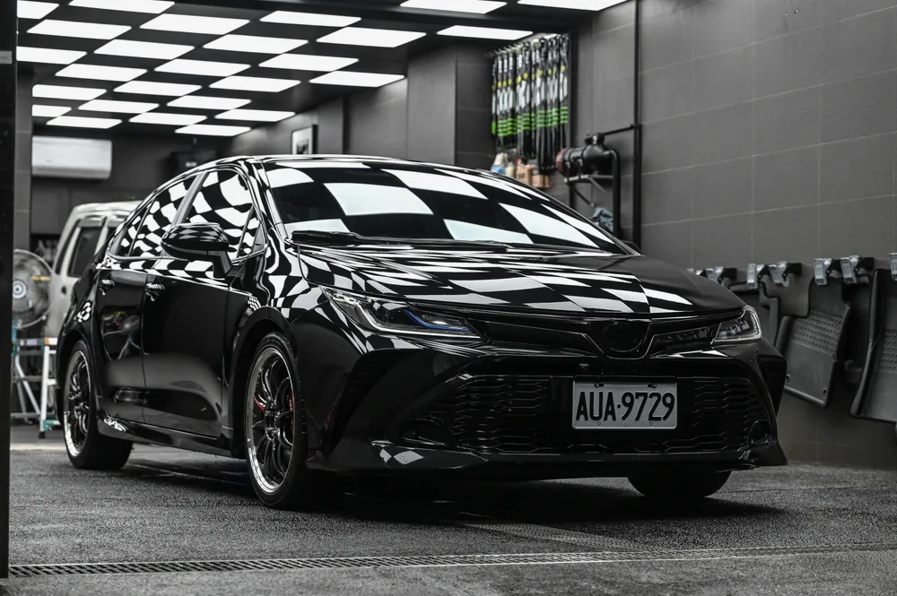 黑色 Toyota 轎車完工後停在棚內,車頭 45 度角漆面映出天花板格紋燈|誠美車體美容