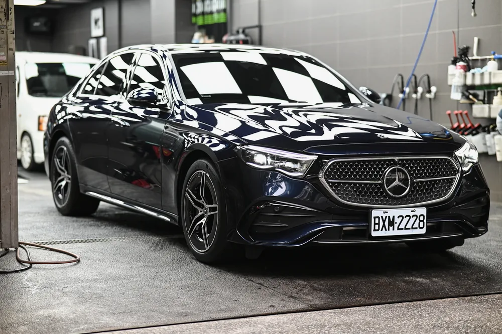 完工後的深藍色 Mercedes-Benz 停在施工區,車頭漆面映出格紋燈光,誠美車體美容