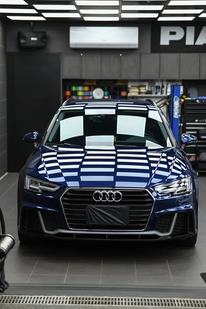 鍍膜完工的深藍色 Audi A4 正面停放於施工區,引擎蓋與水箱護罩映出整排燈條,誠美車體美容