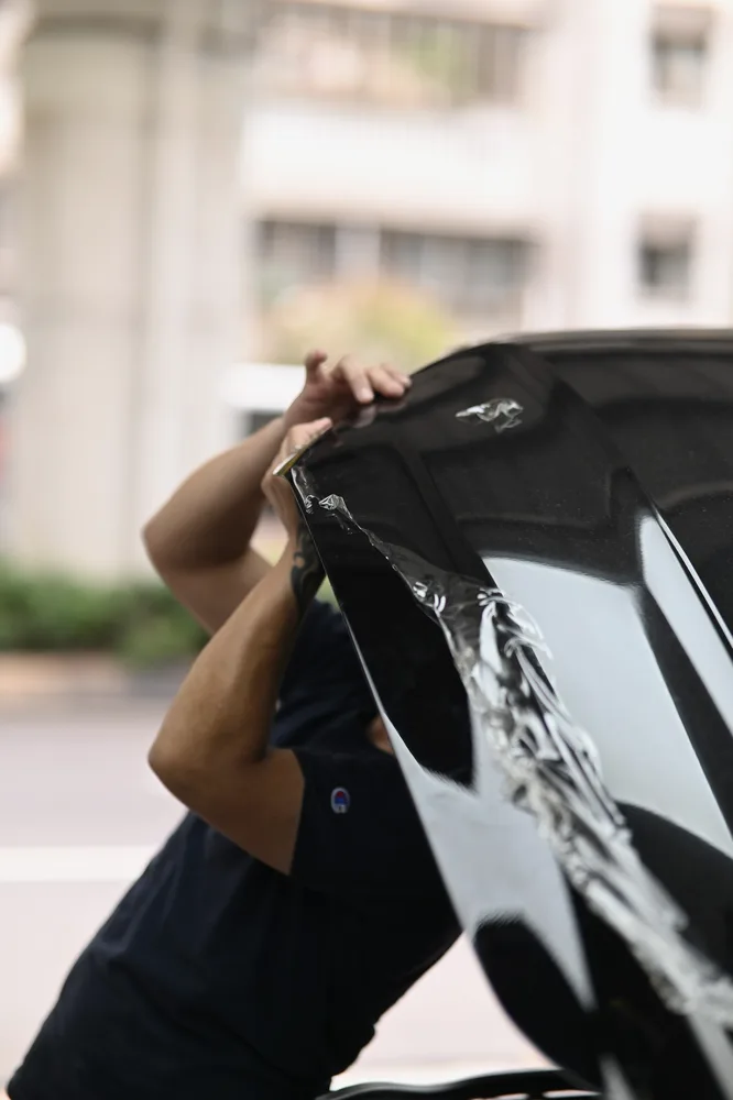 黑色 Ford Mustang 引擎蓋,技師自前緣掀起老化的迎風面保護膜