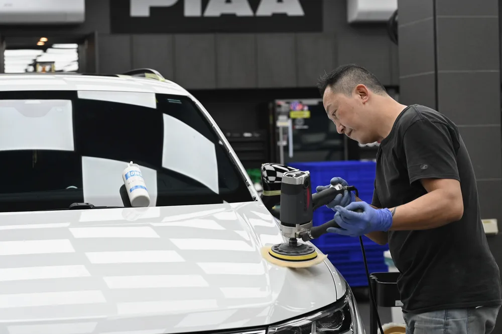 技師以拋光機處理白色休旅車引擎蓋,車頭在燈光下映出格紋倒影,誠美車體美容