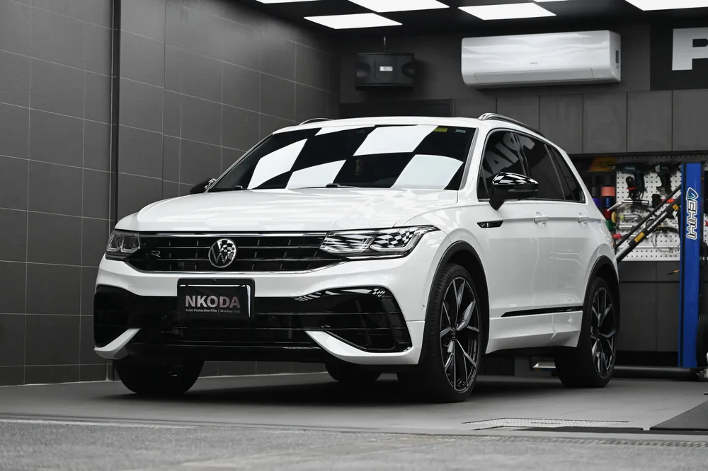 白色 Volkswagen Tiguan 完成車頭迎風面透明保護膜包覆後,停於施工棚內的左前四十五度全車樣貌,誠美車體美容